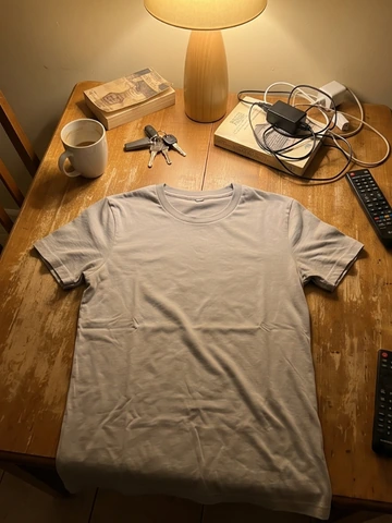 Amateur photo of a grey T-shirt on a cluttered desk under dim lamplight